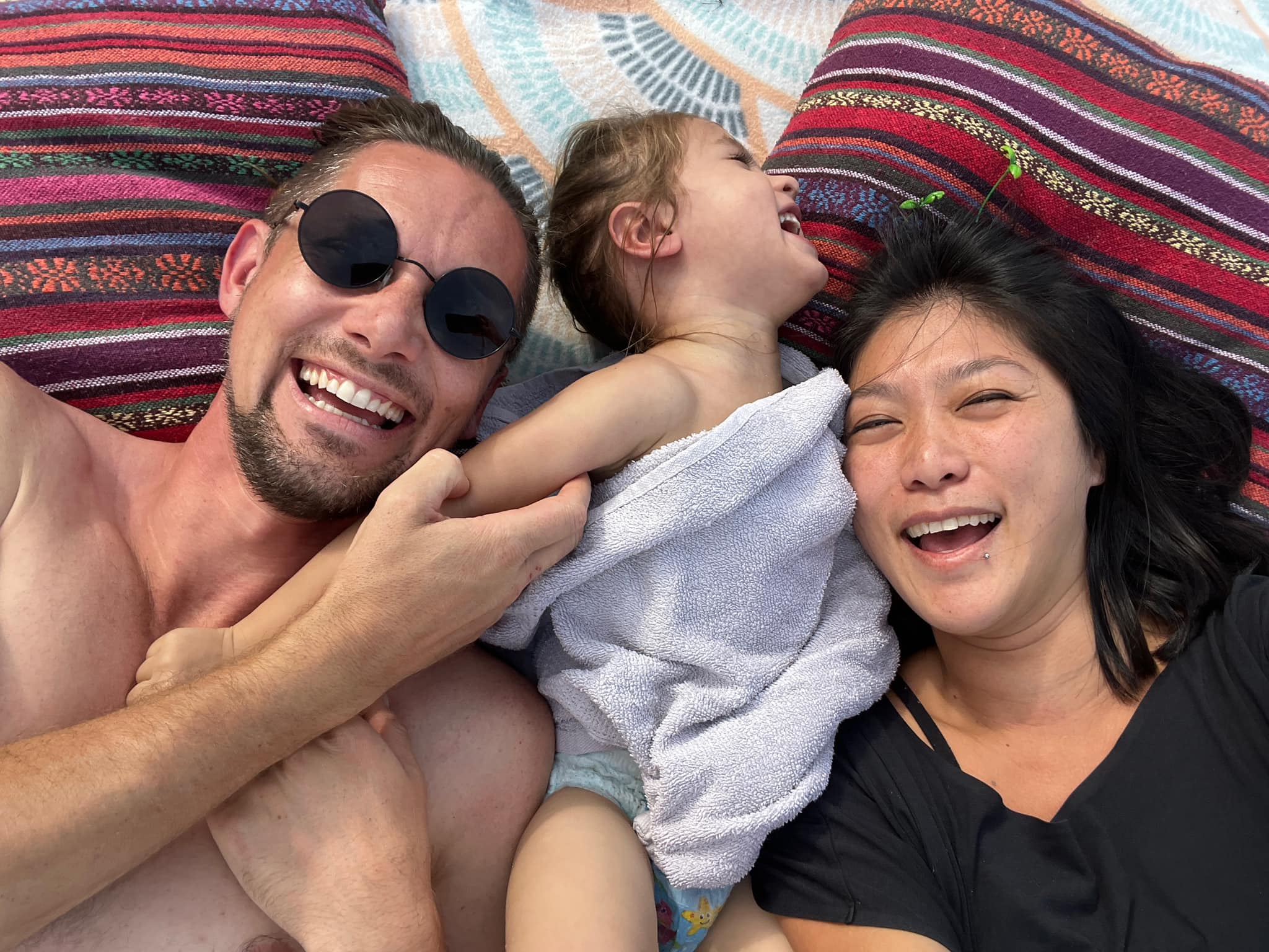 Guy, Tian, and Cosmo laughing together on a colourful blanket